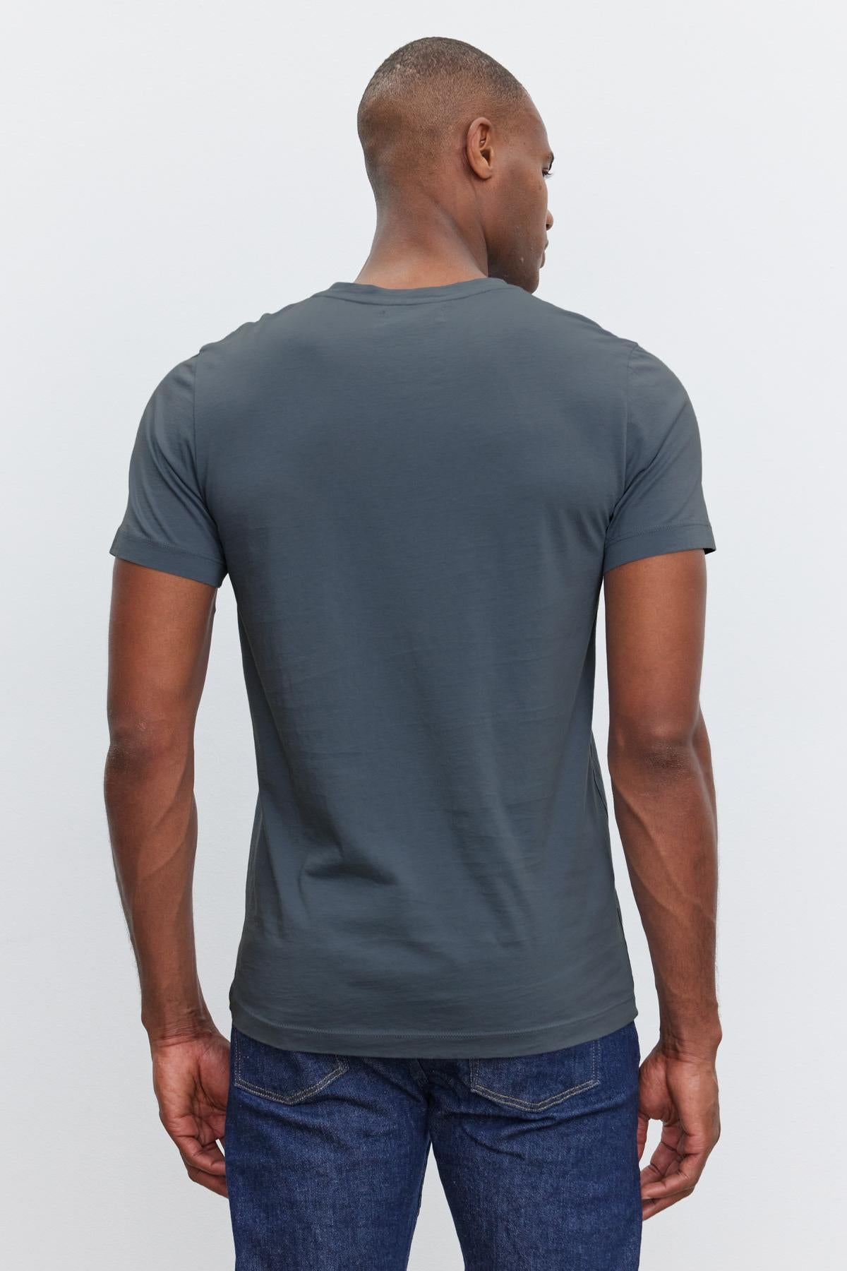   A person wearing a dark gray SAMSEN TEE by Velvet by Graham & Spencer and blue jeans is standing with their back to the camera. 