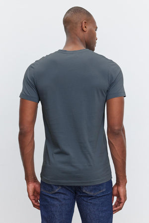 A person wearing a dark gray SAMSEN TEE by Velvet by Graham & Spencer and blue jeans is standing with their back to the camera.