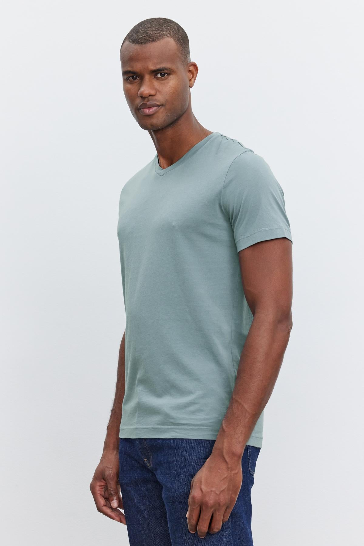   A person with short hair, wearing a light green SAMSEN TEE from Velvet by Graham & Spencer with a v-neckline and blue jeans, stands against a plain white background—a perfect example of everyday wear. 