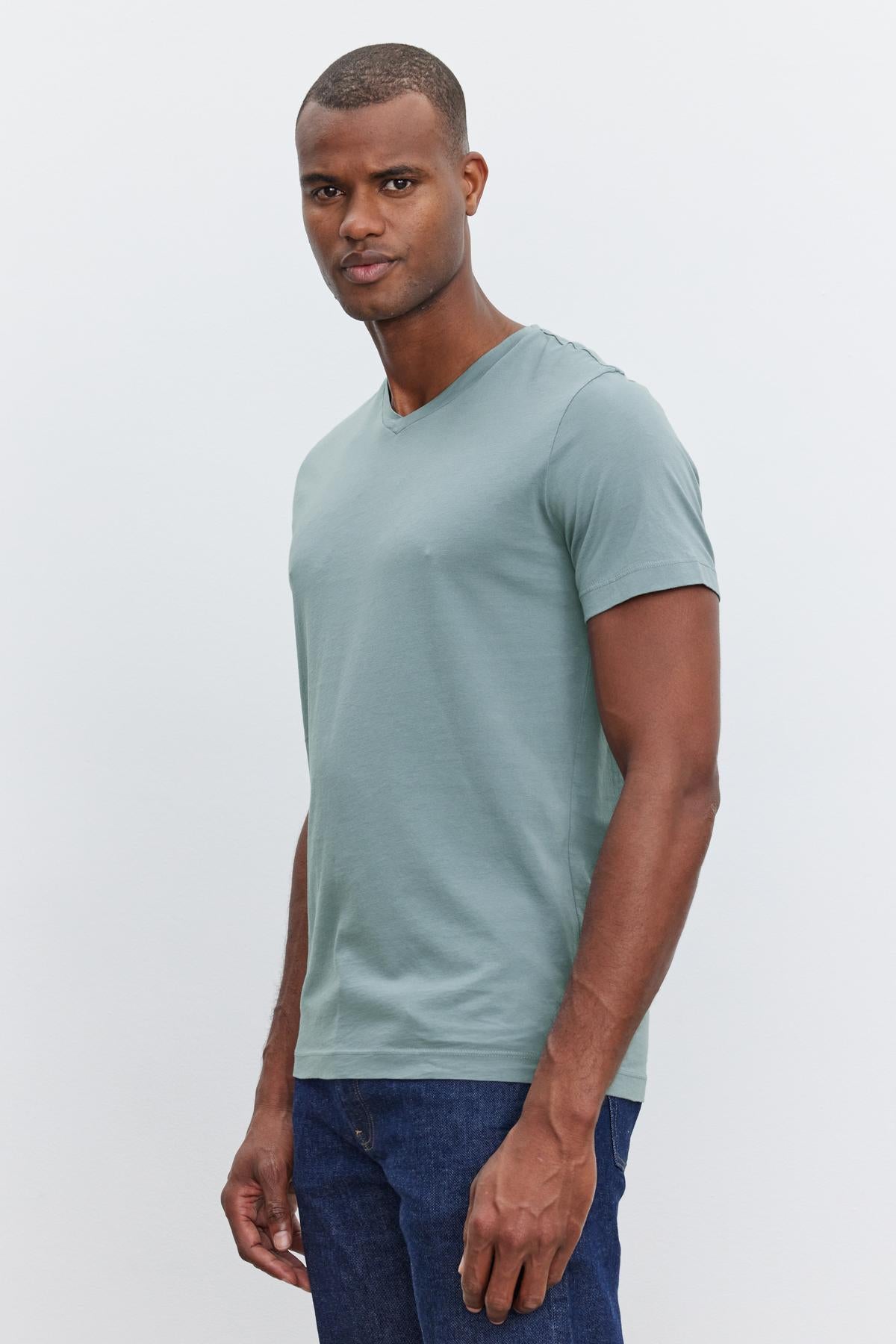 A person with short hair, wearing a light green SAMSEN TEE from Velvet by Graham & Spencer with a v-neckline and blue jeans, stands against a plain white background—a perfect example of everyday wear.-37409982611649