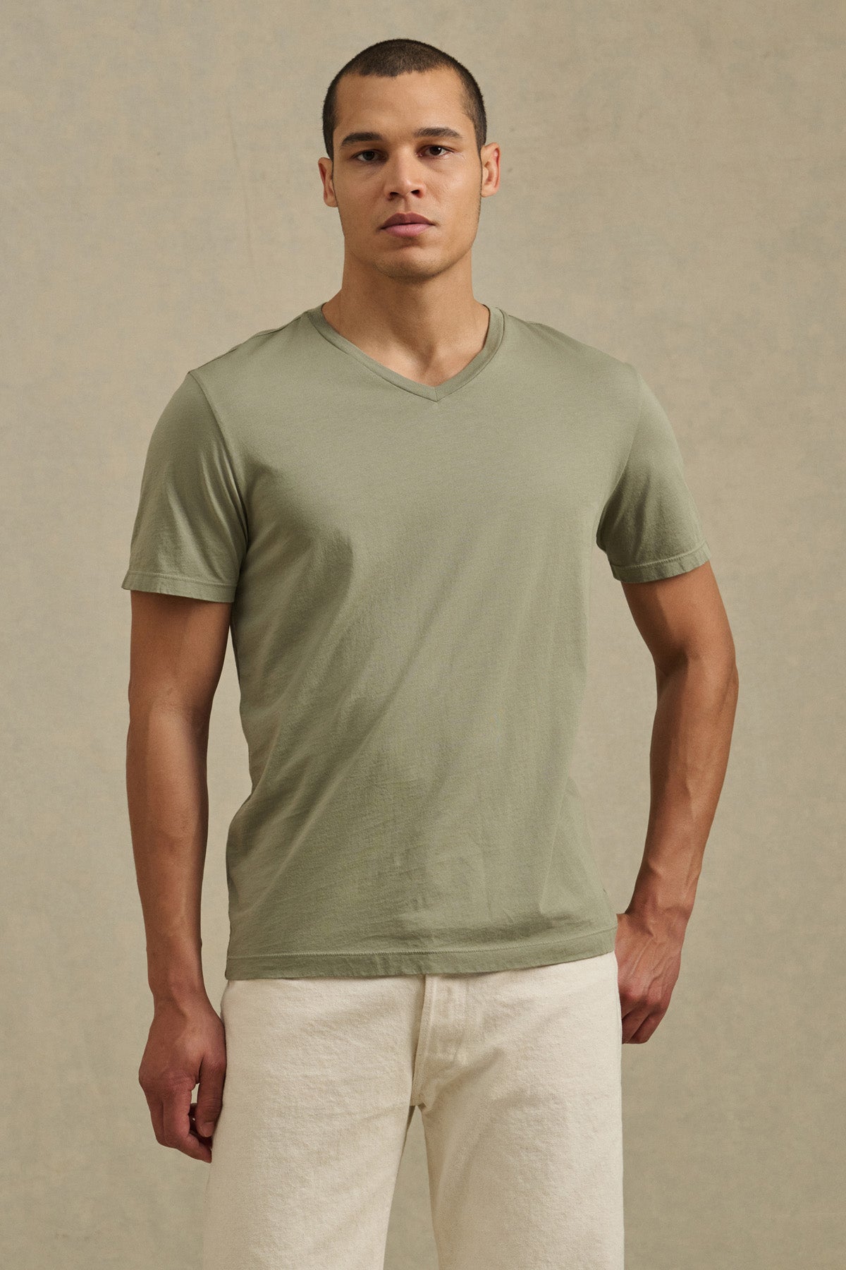 A man poses against a plain background wearing the SAMSEN TEE by Velvet by Graham & Spencer—a light green Pima jersey v-neck shirt—paired with off-white pants, ideal for everyday wear.