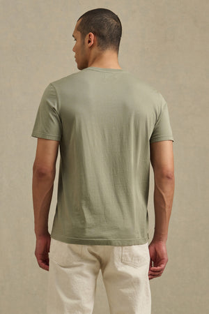 A man faces away, wearing the light green SAMSEN TEE by Velvet by Graham & Spencer with off-white pants—perfect for everyday wear—set against a plain, neutral background.