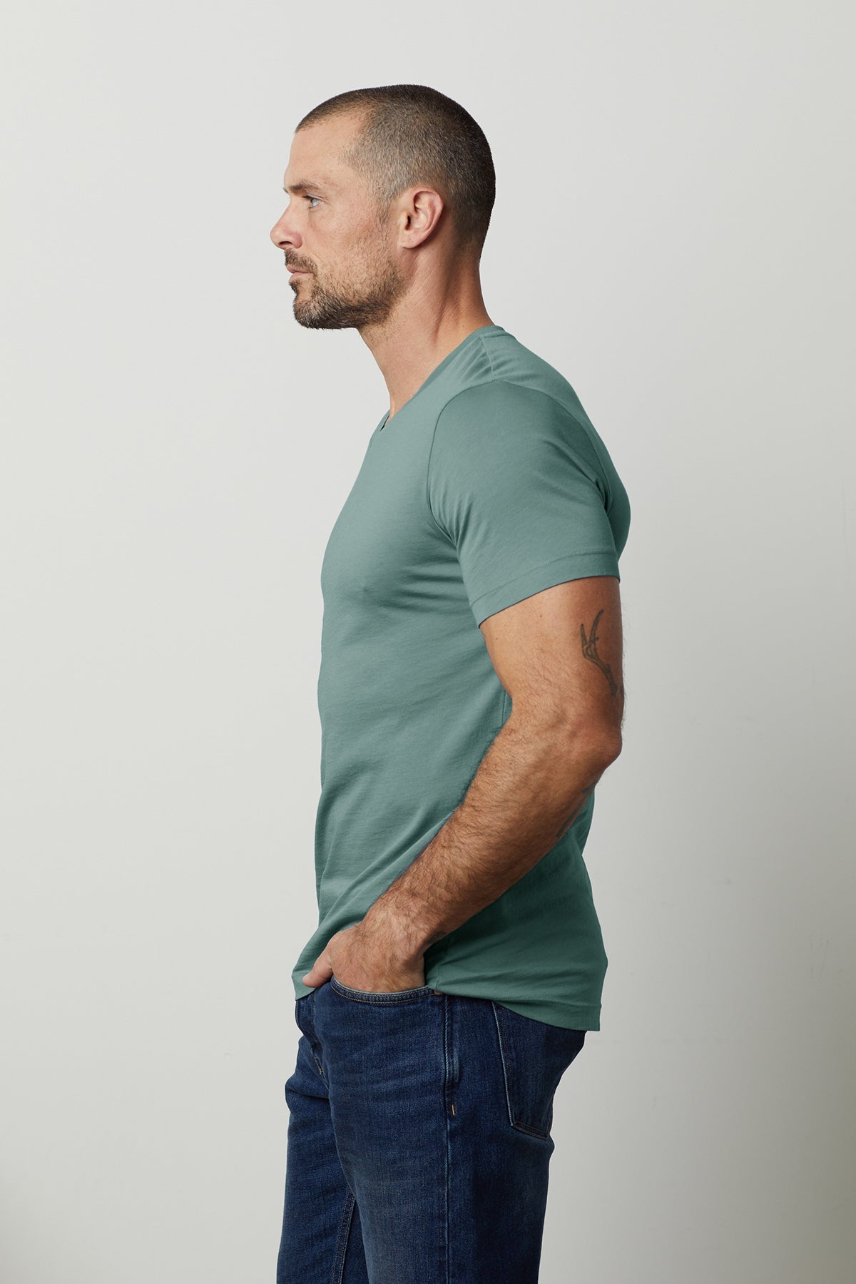 A man wearing jeans and a green SAMSEN WHISPER CLASSIC V-NECK TEE by Velvet by Graham & Spencer.-26496252903617