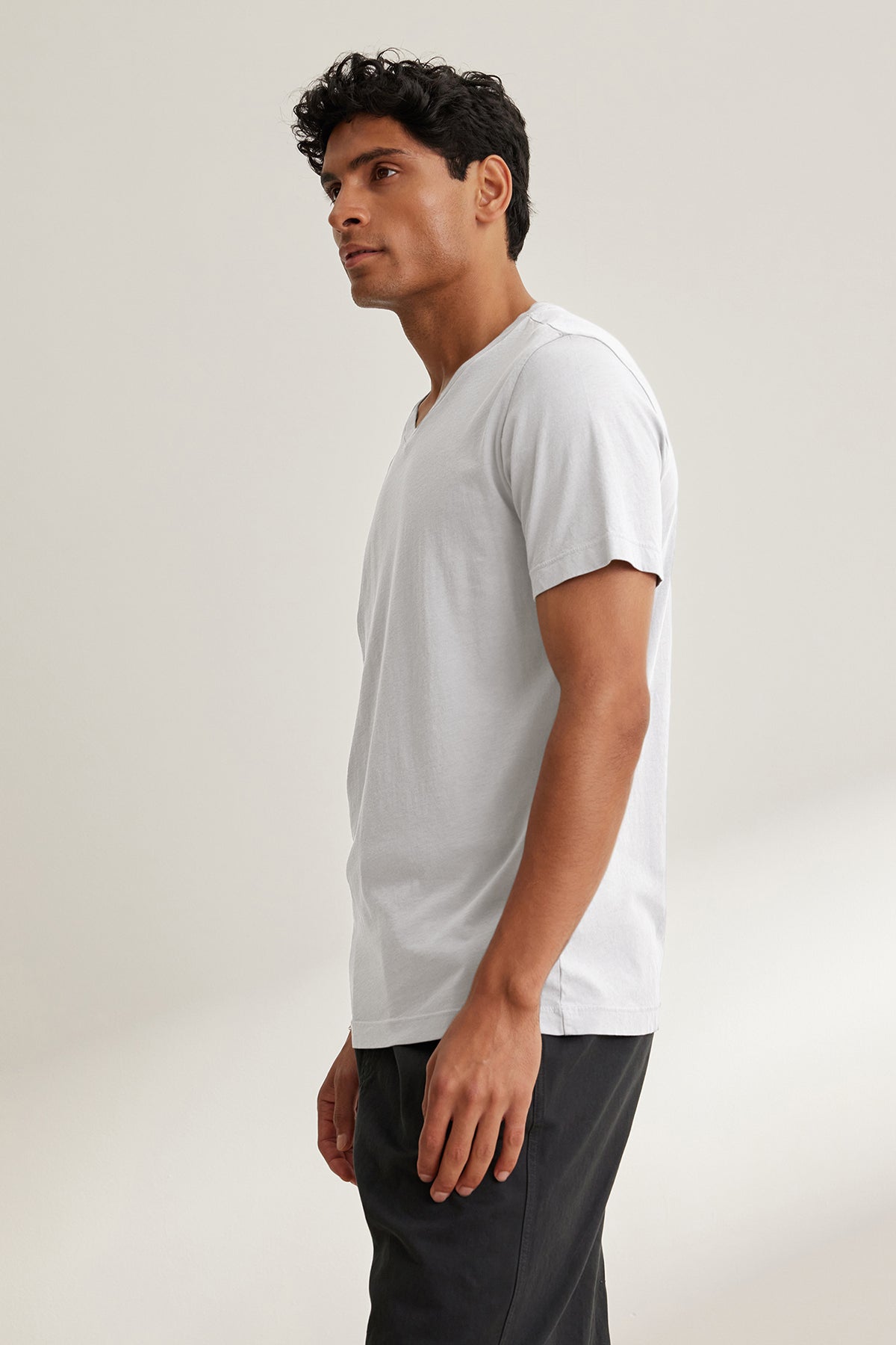   A person in a white SAMSEN TEE from Velvet by Graham & Spencer paired with dark pants looks to the side against a plain backdrop, epitomizing effortless everyday wear. 