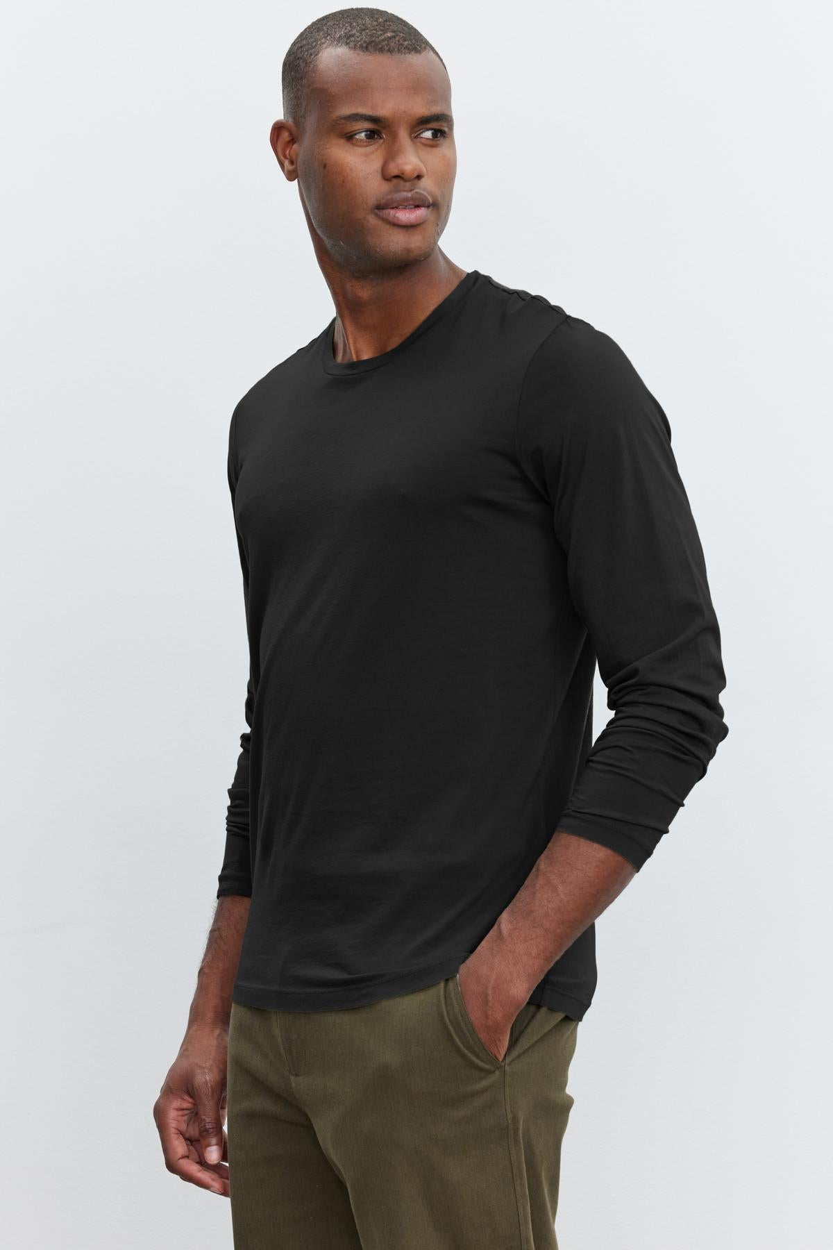   A man in a SKEETER WHISPER CLASSIC CREW NECK TEE by Velvet by Graham & Spencer and olive pants stands against a plain background, looking to the side. 