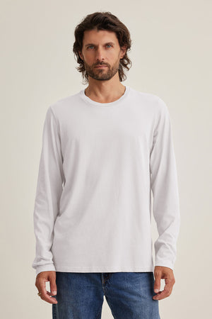 A man in a white SKEETER TEE by Velvet by Graham & Spencer, made from soft Pima jersey, and blue jeans stands facing forward against a neutral background.