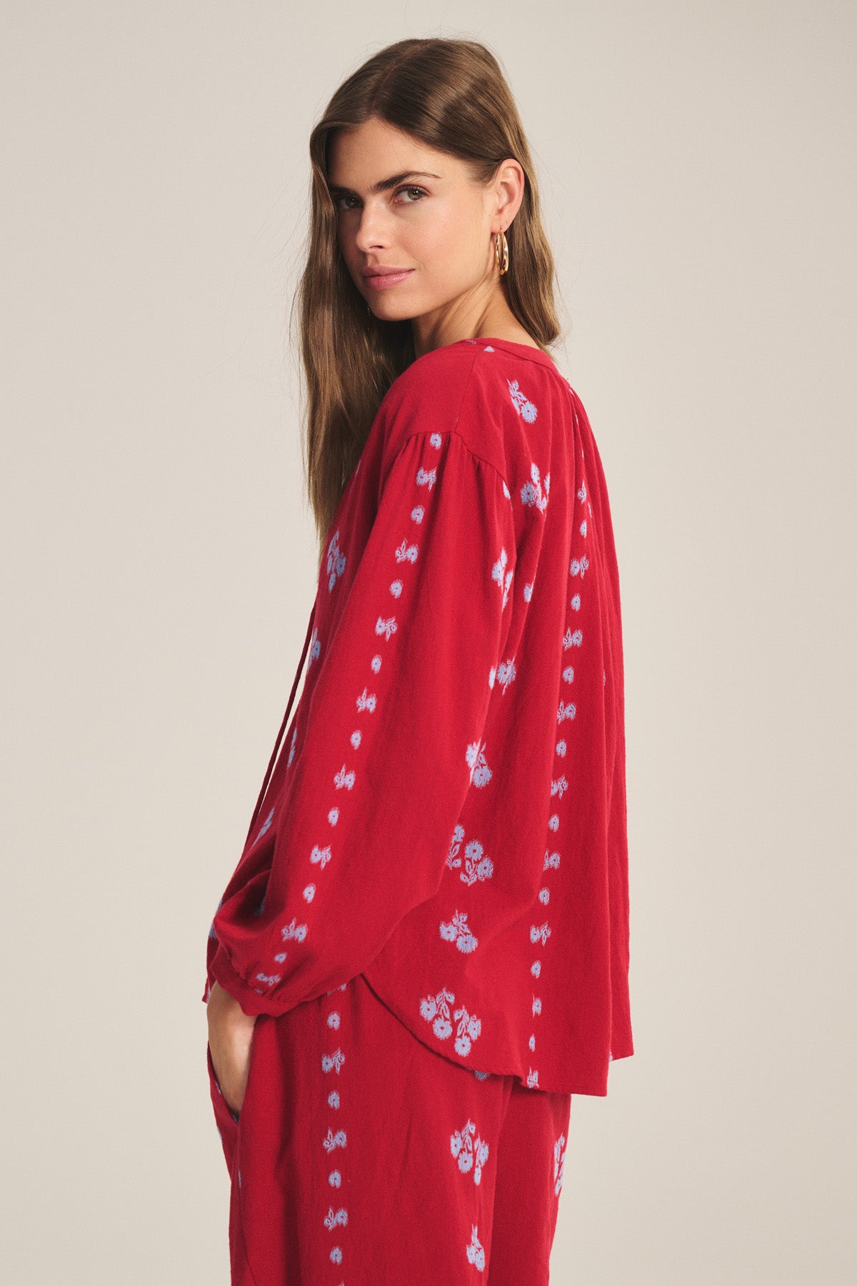 Woman with long brown hair wears the WINSLET TOP by Velvet by Graham & Spencer—a relaxed-fit red cotton jacquard top with blue floral patterns—while looking at the camera against a plain background.-41089089994945