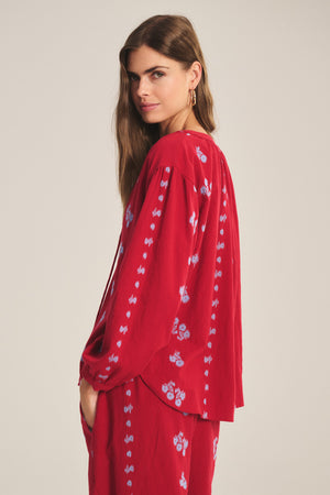 Woman with long brown hair wears the WINSLET TOP by Velvet by Graham & Spencer—a relaxed-fit red cotton jacquard top with blue floral patterns—while looking at the camera against a plain background.