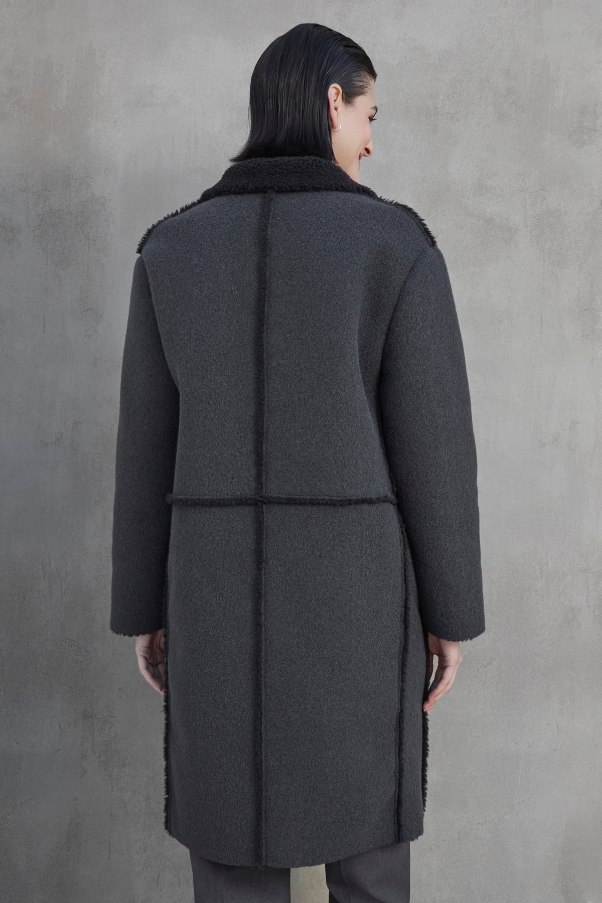   A person with dark hair wearing the ROSEMEAD COAT by Velvet by Jenny Graham stands facing away from the camera against a light grey textured background. 