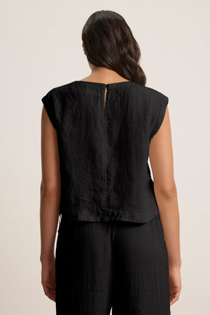 A woman is seen from behind wearing the TAVIA LINEN TOP by Velvet by Graham & Spencer in black, featuring a boxy cropped fit, paired with matching black pants against a plain, light background.