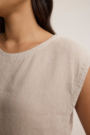 Close-up of a person wearing the TAVIA LINEN TOP by Velvet by Graham & Spencer, a beige, short-sleeve cropped linen piece highlighting the neckline and shoulder—an effortlessly breathable choice for warm days.