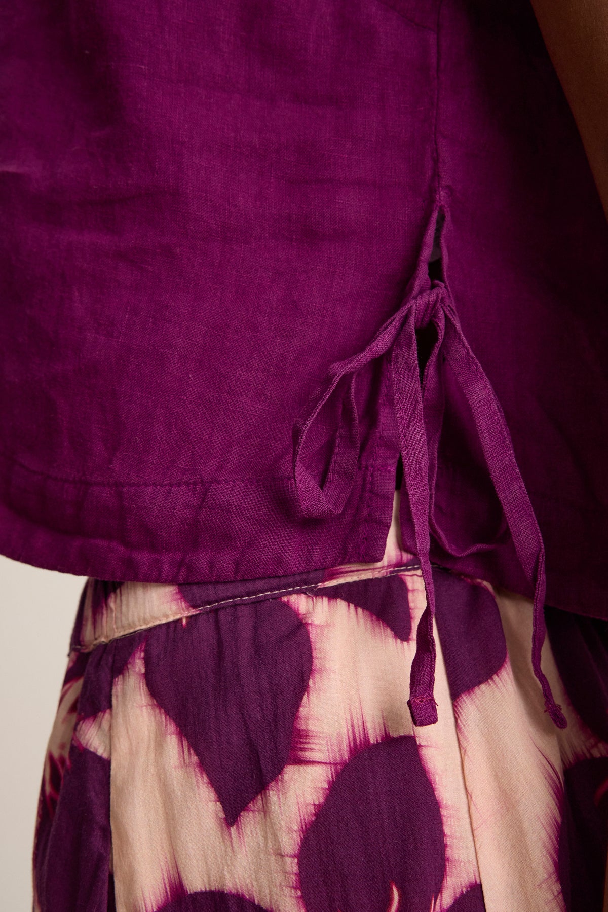 Close-up of a person wearing the TAVIA LINEN TOP by Velvet by Graham & Spencer, featuring side ties and paired with cream and purple patterned pants for a flowy silhouette.-39111856718017
