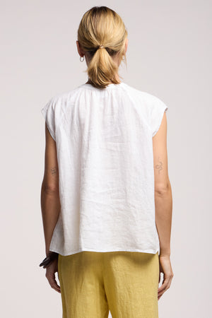 A person with blonde hair in a low ponytail is shown from the back, wearing the BEC LINEN TOP by Velvet by Graham & Spencer and yellow pants.