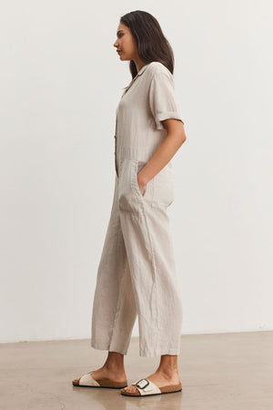 A woman in a Velvet by Graham & Spencer DELILAH LINEN JUMPSUIT and sandals stands profiled in a minimalist indoor setting.