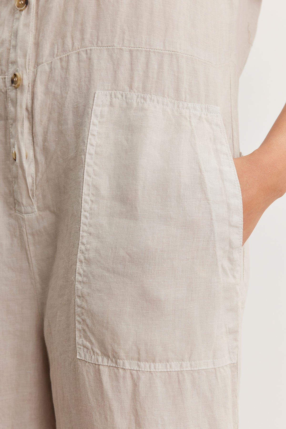   Close-up of a beige Velvet by Graham & Spencer Delilah linen jumpsuit with a detailed view of its side pocket and button line. 