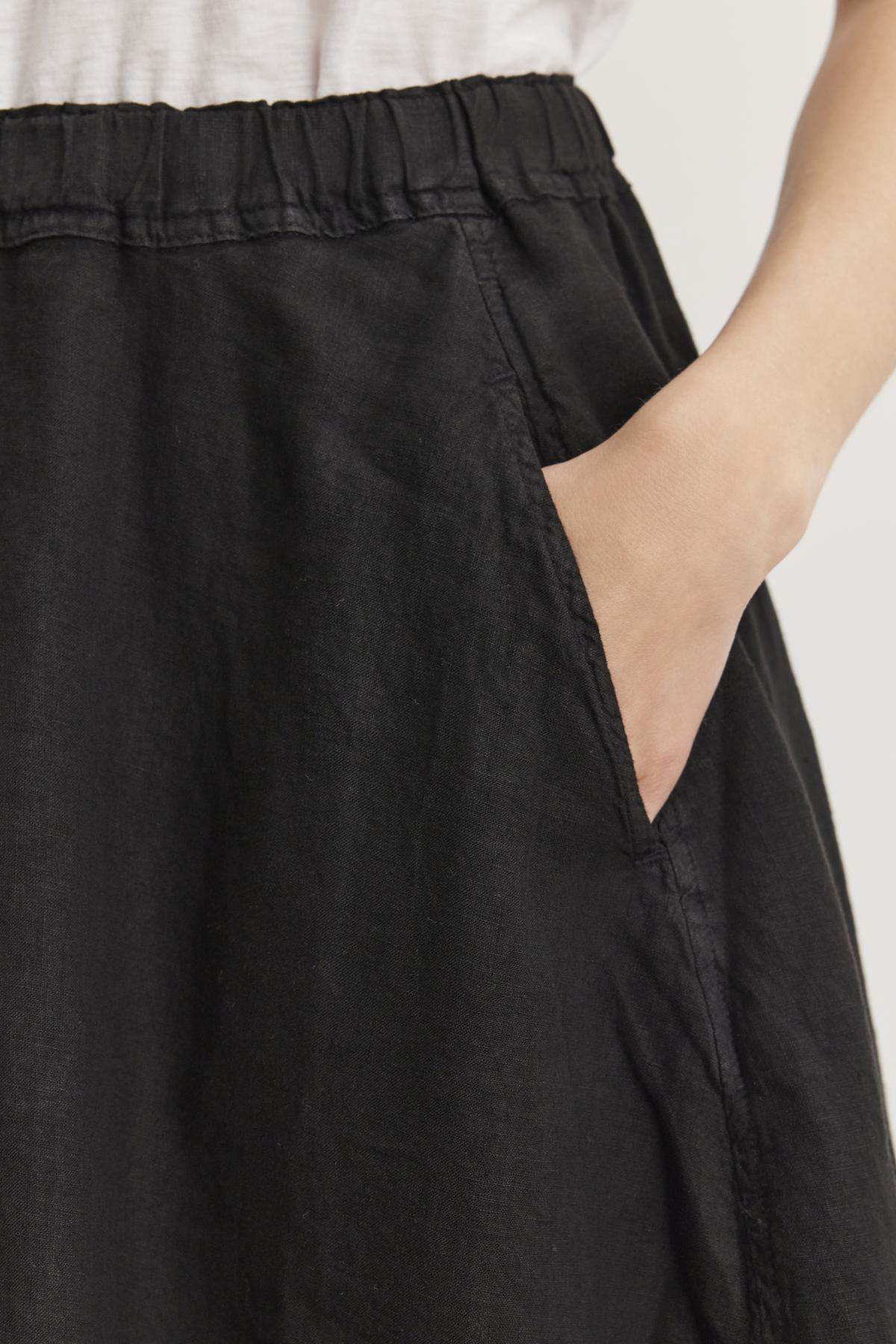   Close-up of a person wearing the FAE LINEN SKIRT by Velvet by Graham & Spencer, made from spring-weight linen with an elastic waistband, with their right hand placed in the pocket of the skirt. 