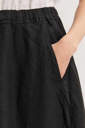 Close-up of a person wearing the FAE LINEN SKIRT by Velvet by Graham & Spencer, made from spring-weight linen with an elastic waistband, with their right hand placed in the pocket of the skirt.