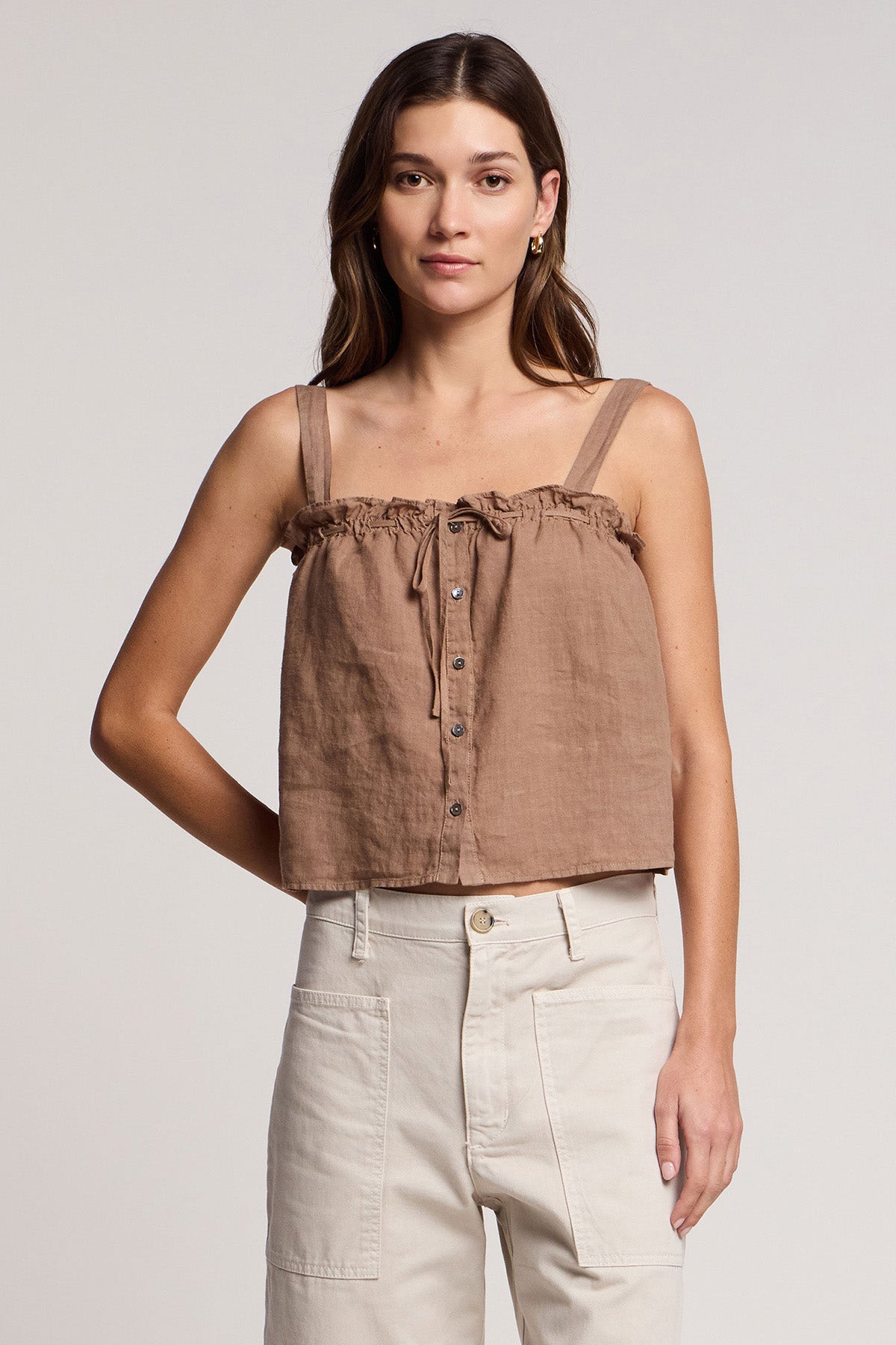 A woman faces forward, wearing the Velvet by Graham & Spencer IZZIE LINEN TANK TOP—a brown, lightweight woven linen cropped tank with adjustable fit—and high-waisted light beige pants against a plain background.-41527050240193