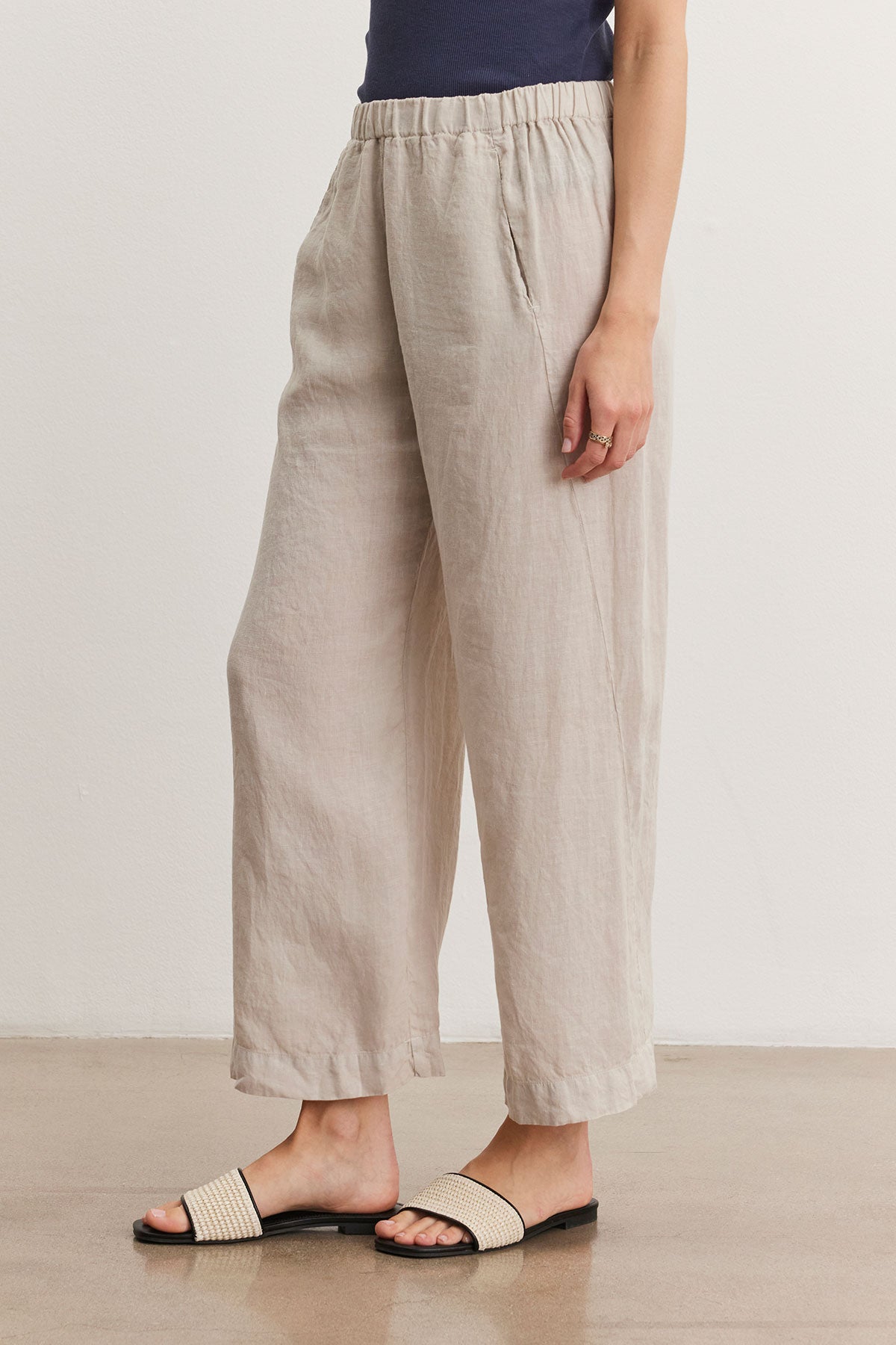   Person wearing Velvet by Graham & Spencer's LOLA LINEN PANT with pockets, a dark-colored top, and black-and-beige sandals. They are standing on a light-colored floor, with the focus on the lower half of their body. 