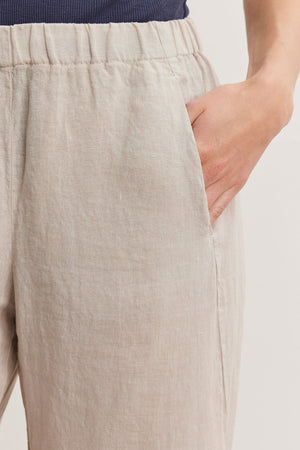 Close-up of a person wearing Velvet by Graham & Spencer LOLA LINEN PANT with an elastic waistband and a hidden side pocket. The person has one hand in the pocket.