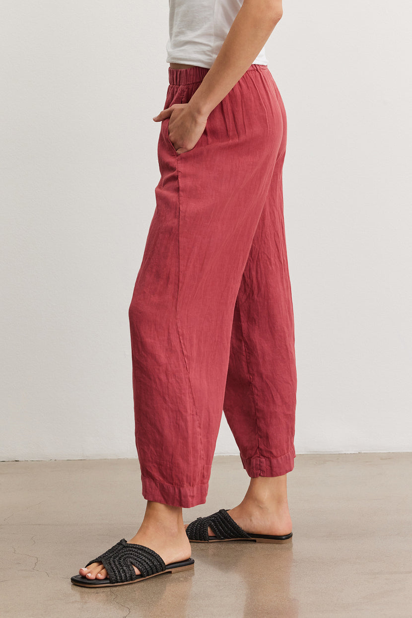 Side view of a person wearing red Velvet by Graham & Spencer LOLA LINEN PANT and black slide sandals on a neutral background.