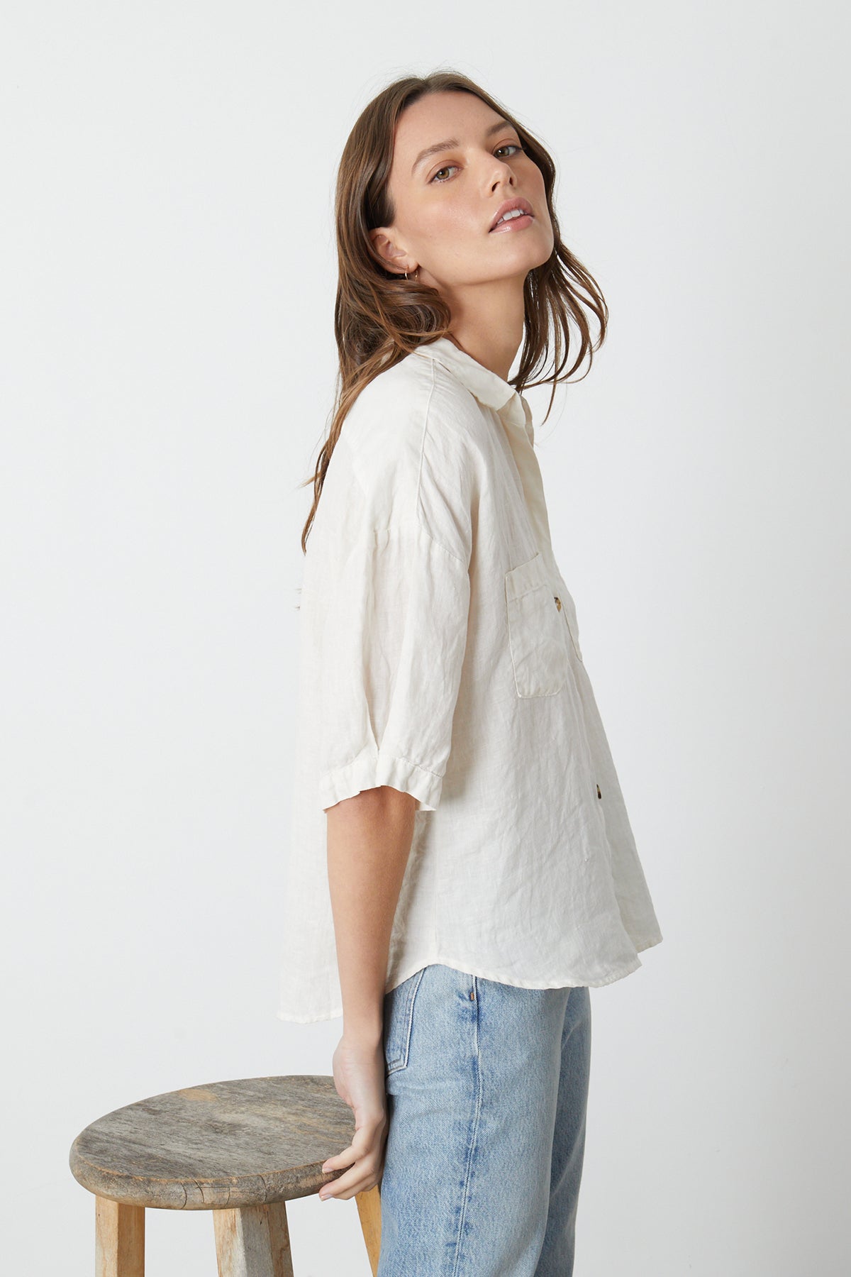   The model is wearing a white MARIA LINEN BUTTON-UP SHIRT by Velvet by Graham & Spencer and jeans. 