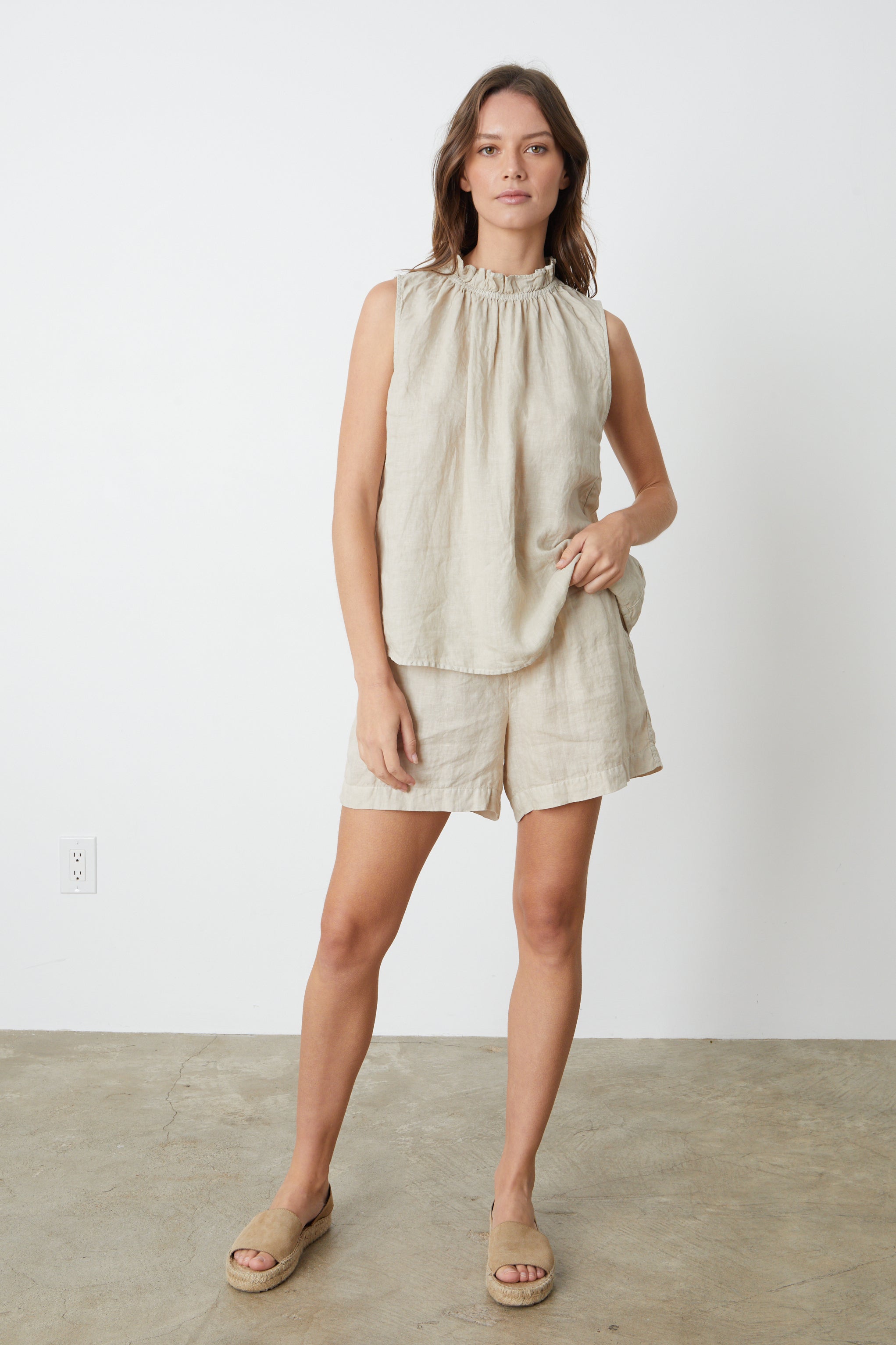   A woman wearing a sleeveless NOVA LINEN TOP by Velvet by Graham & Spencer and shorts in sand full length front shot with sandals. 