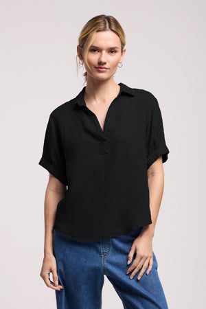 Dressed in Velvet by Graham & Spencer’s VIVICA LINEN TOP—a short-sleeve black collared shirt—paired with blue jeans, this look stands out against a plain light background as the ideal warm-weather ensemble. The lightweight linen and subtle split neckline bring effortless comfort and relaxed style to any summer day.