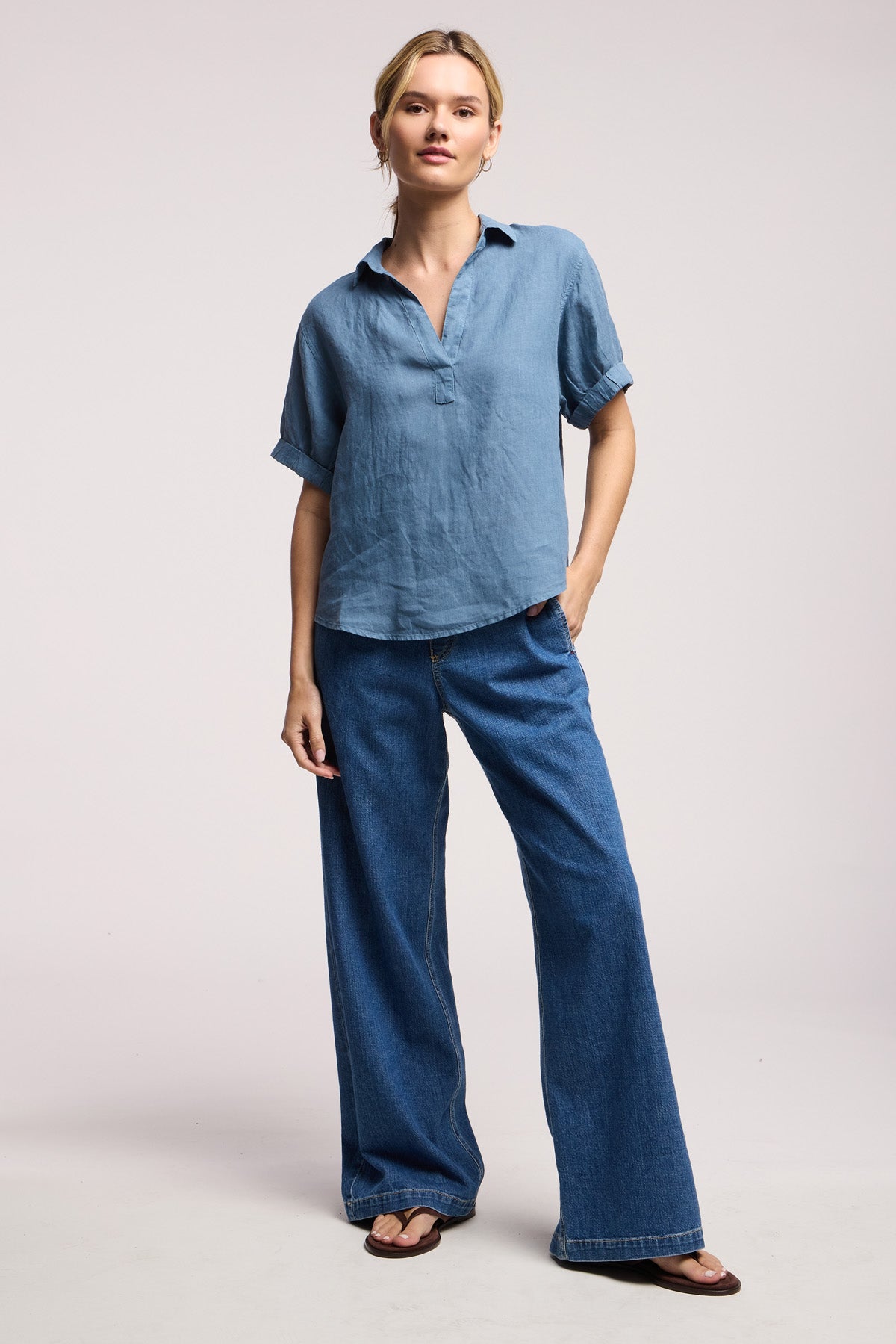 A person stands against a plain background wearing the VIVICA LINEN TOP by Velvet by Graham & Spencer, paired with wide-leg blue jeans and sandals—an ideal outfit for warm-weather days.-41372267118785