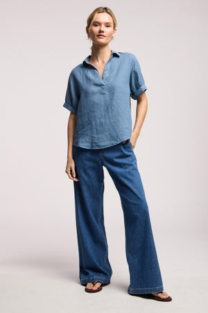 A person stands against a plain background wearing the VIVICA LINEN TOP by Velvet by Graham & Spencer, paired with wide-leg blue jeans and sandals—an ideal outfit for warm-weather days.