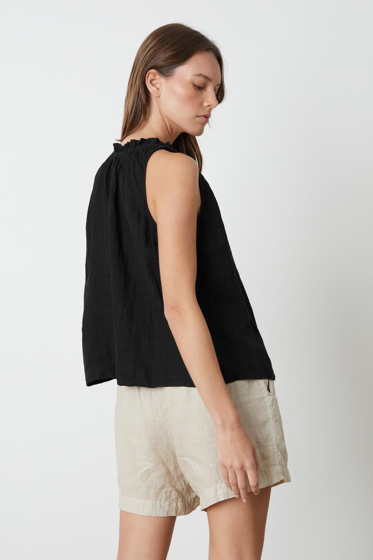 The back view of a woman wearing the Velvet by Graham & Spencer Zoey Linen V-Neck Tank Top and beige shorts.-35201191674049