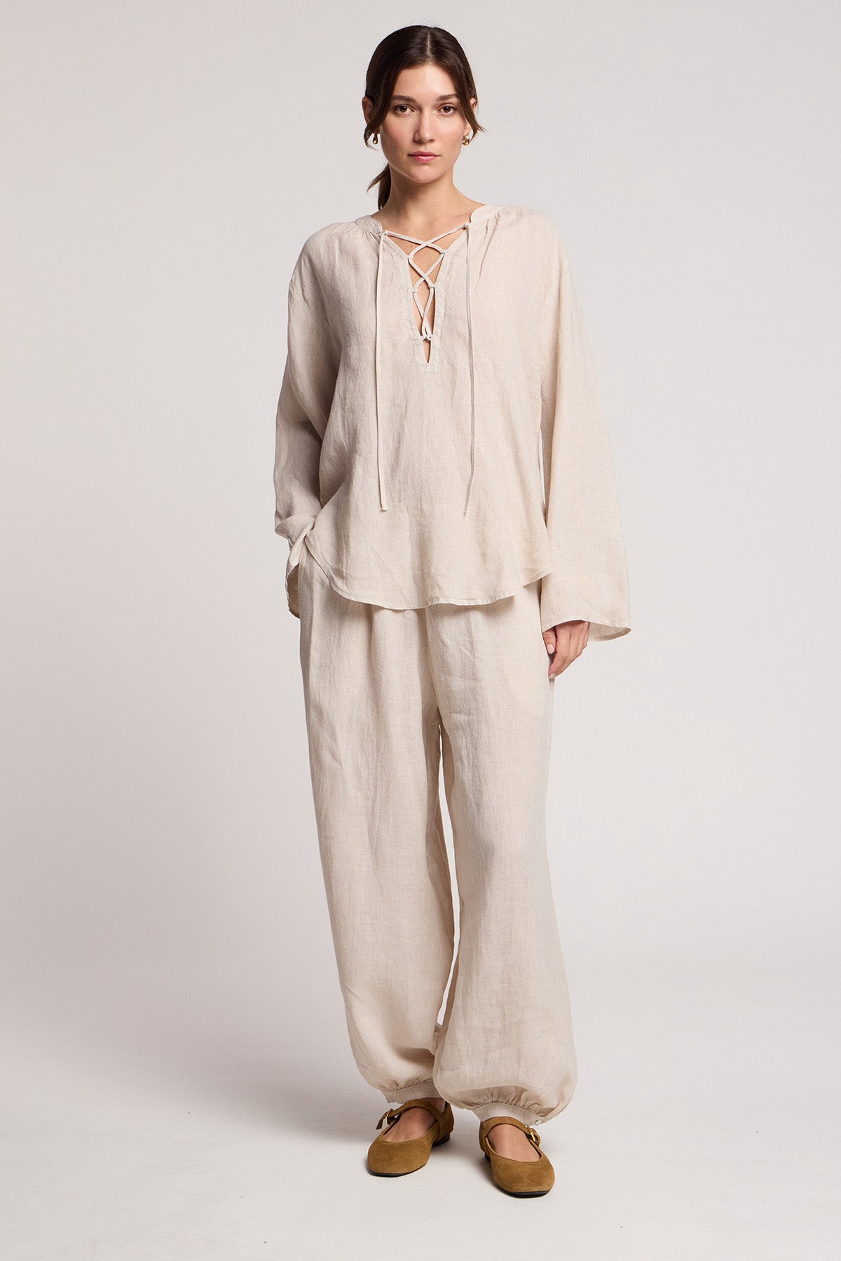 A woman stands in a studio wearing Velvet by Graham & Spencer's CAMBER LINEN PANT with an elastic waist, paired with a loose-fitting woven linen top and brown flats.-41371565031617