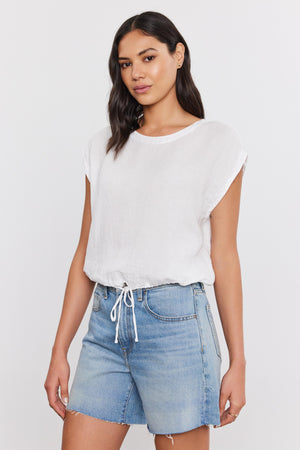 Woman wearing a BAYLA LINEN TOP from Velvet by Graham & Spencer with a scoop neckline and blue denim shorts standing against a plain background.