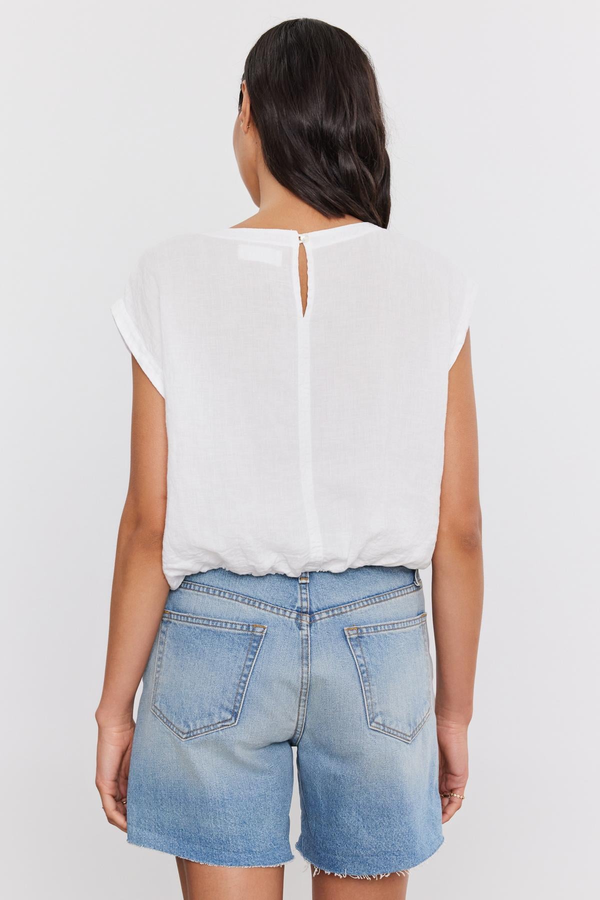   Woman from behind wearing a BAYLA LINEN TOP by Velvet by Graham & Spencer with a scoop neckline and blue denim shorts. 