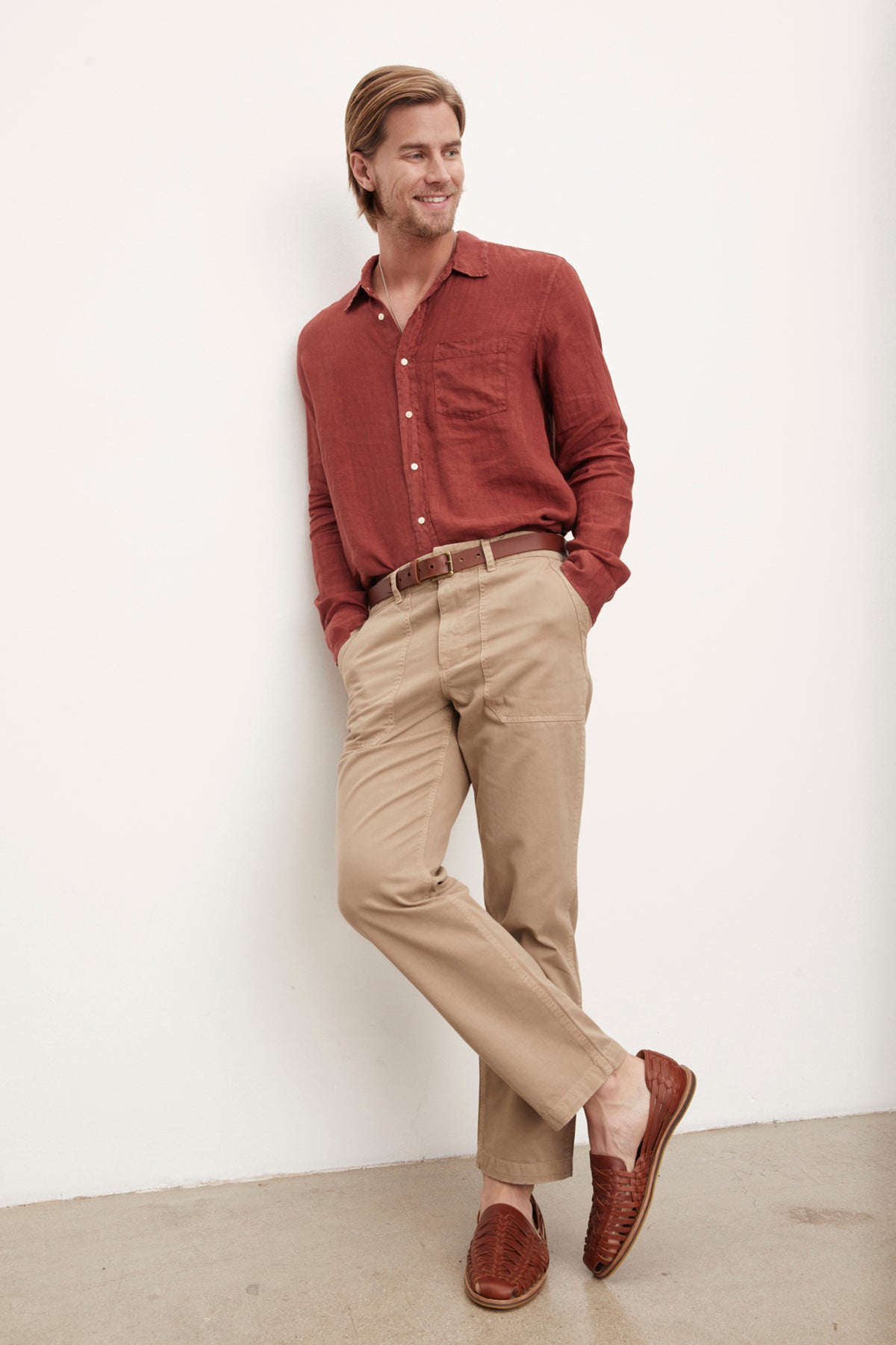   A stylish man wearing a Velvet by Graham & Spencer BENTON LINEN BUTTON-UP SHIRT and khaki pants leaning against a wall. 