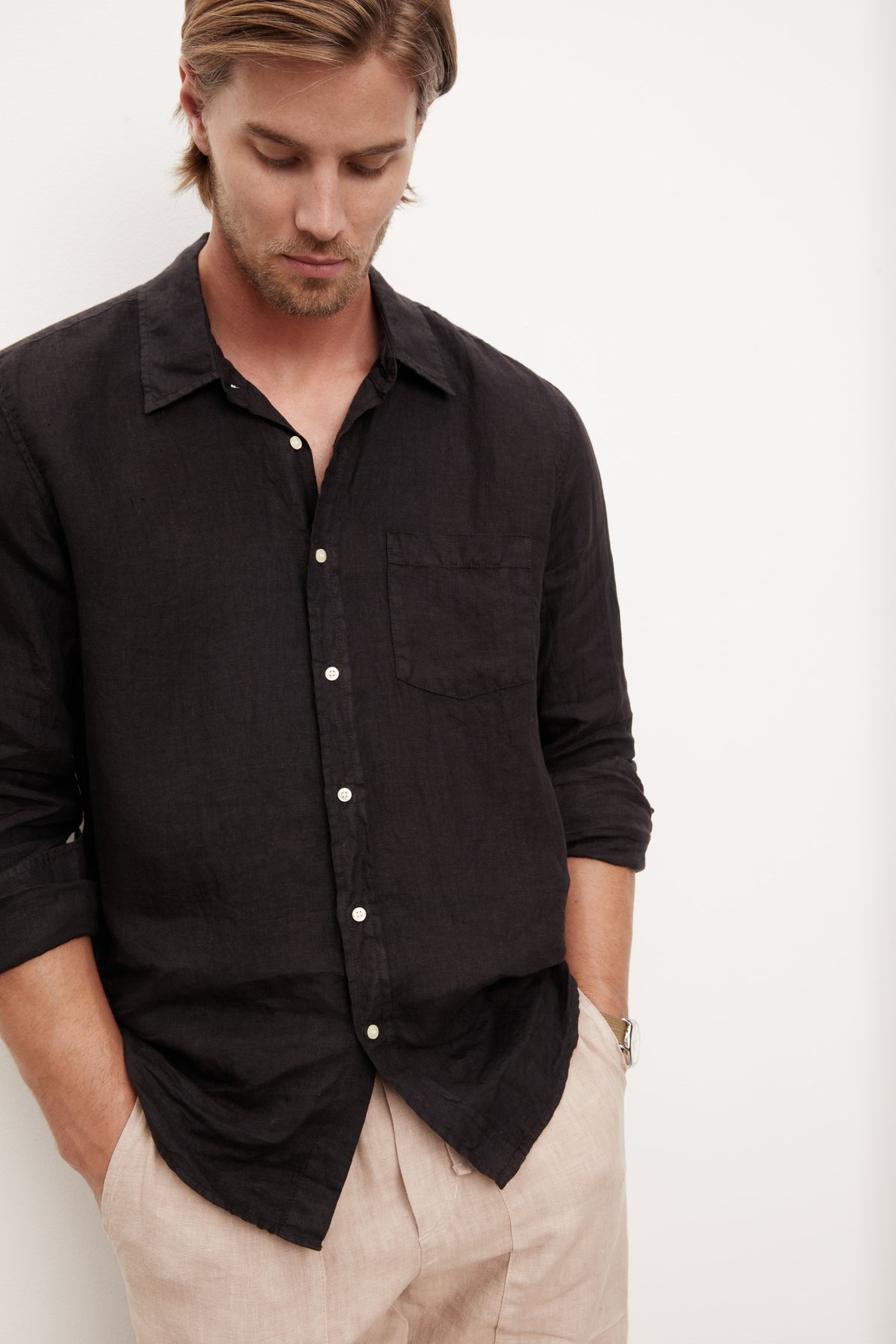 A stylish man in a Velvet by Graham & Spencer BENTON LINEN BUTTON-UP SHIRT leaning against a wall.-36009360425153