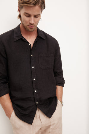 A stylish man in a Velvet by Graham & Spencer BENTON LINEN BUTTON-UP SHIRT leaning against a wall.