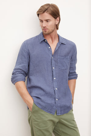 A stylish man in a Velvet by Graham & Spencer men's blue woven Benton Linen Button-Up Shirt leaning against a wall.