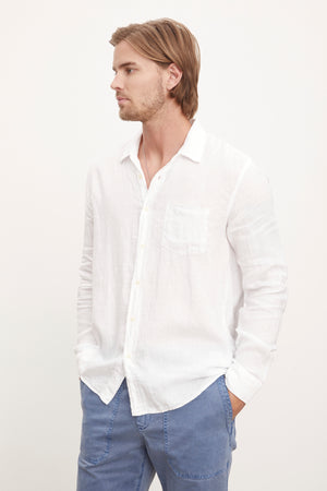 A stylish man sporting a white Velvet by Graham & Spencer Benton Linen Button-Up Shirt and blue pants.