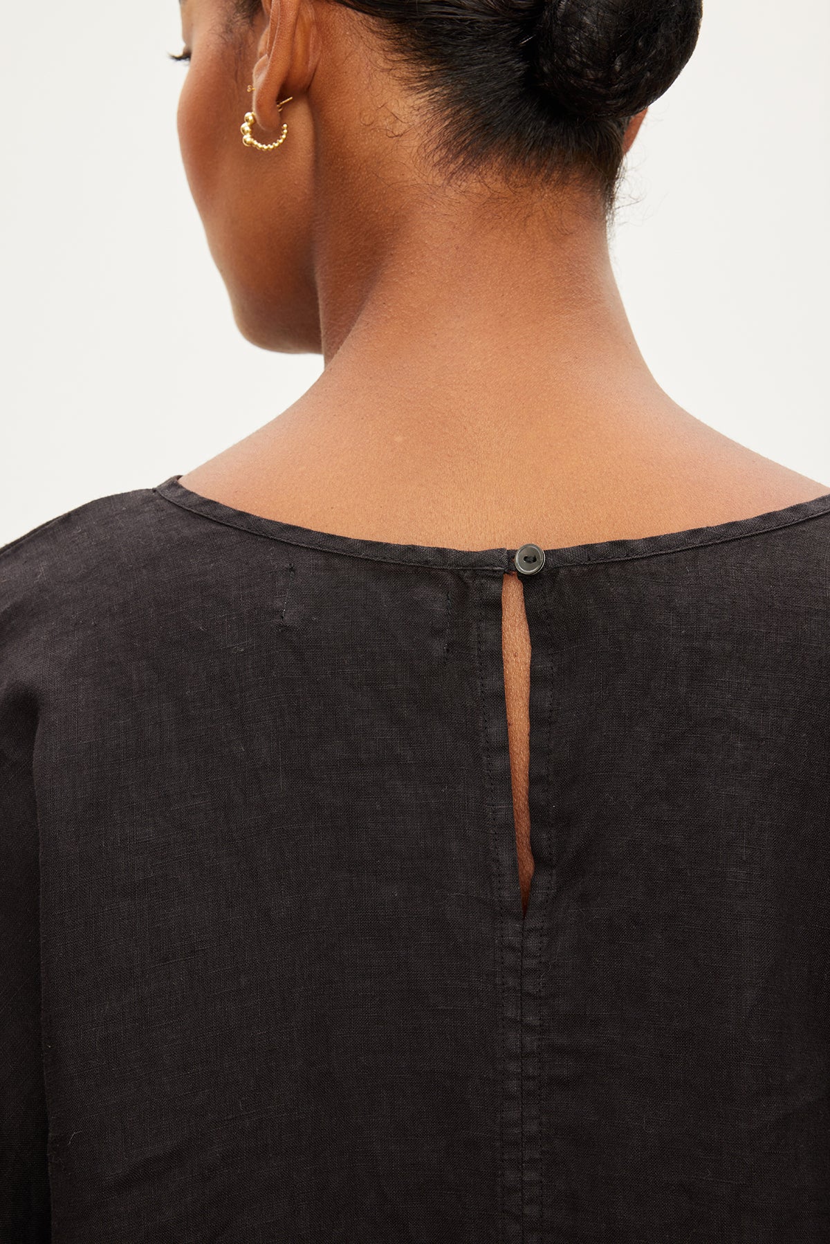 A woman's back with a Velvet by Graham & Spencer CASS LINEN CREW NECK TOP black shirt with a twist knot.-35955522797761