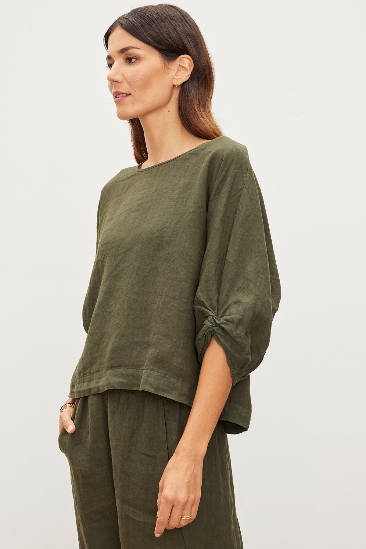   A woman in a loose-fitting green CASS LINEN TOP by Velvet by Graham & Spencer, featuring a cocoon silhouette, stands against a plain background. 