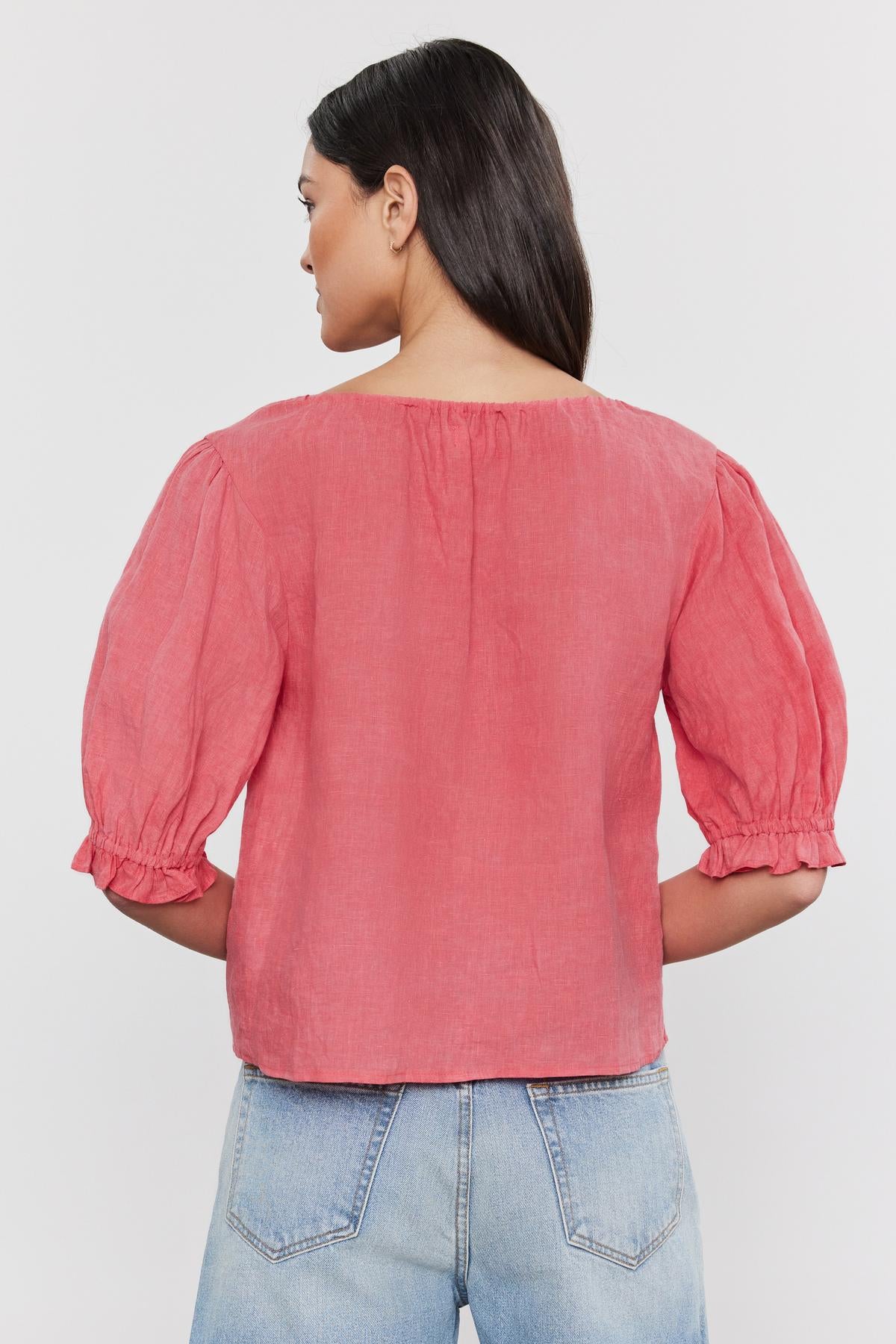   Woman pictured from behind wearing a Velvet by Graham & Spencer CELINE LINEN TOP with puff sleeves and blue jeans, standing against a white background. 