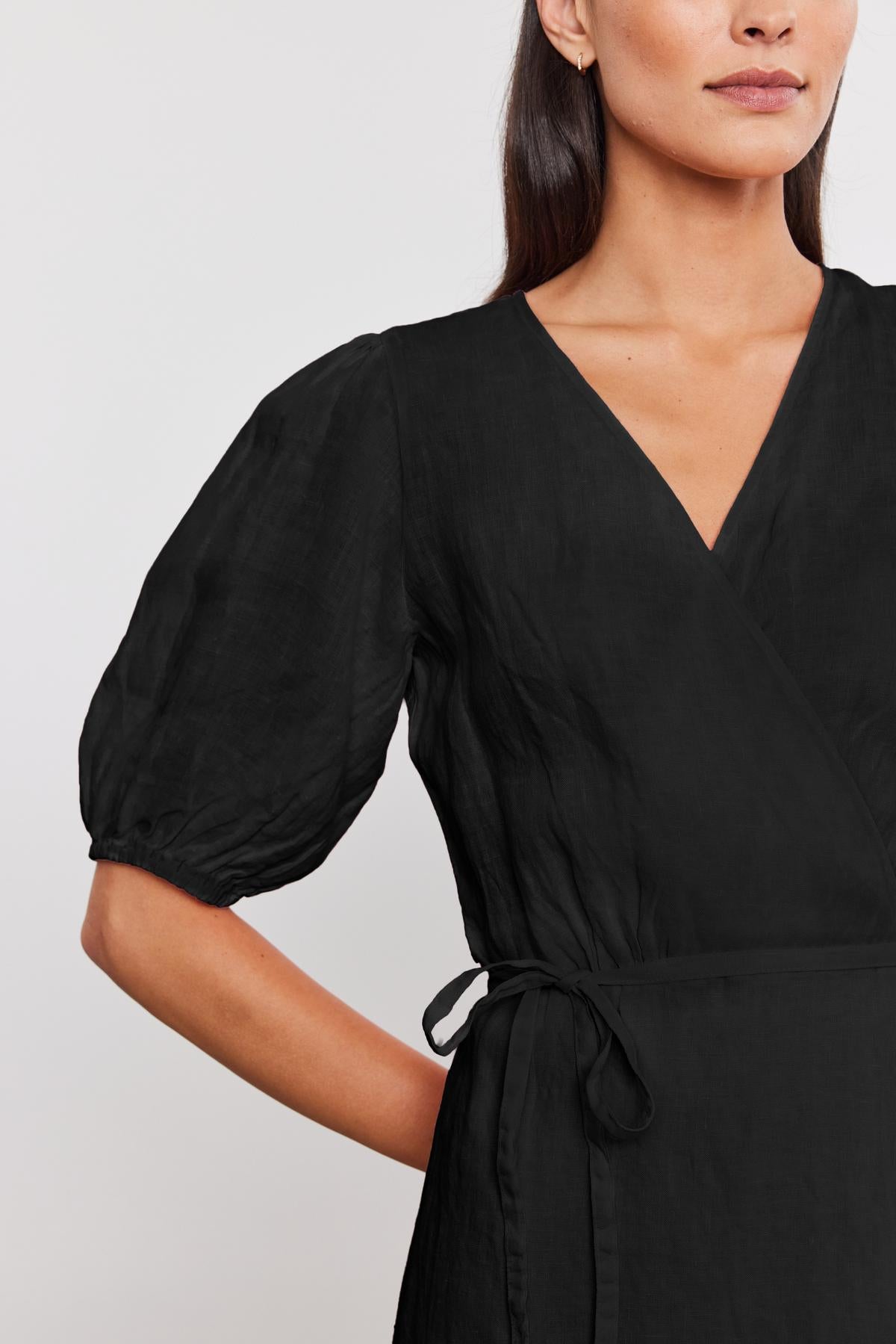 Woman wearing a black v-neck wrap Dalede Linen Dress with puffed sleeves and a tie at the waist, cropped view focusing on the upper body.-36917057945793