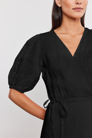 Woman wearing a black v-neck wrap Dalede Linen Dress with puffed sleeves and a tie at the waist, cropped view focusing on the upper body.