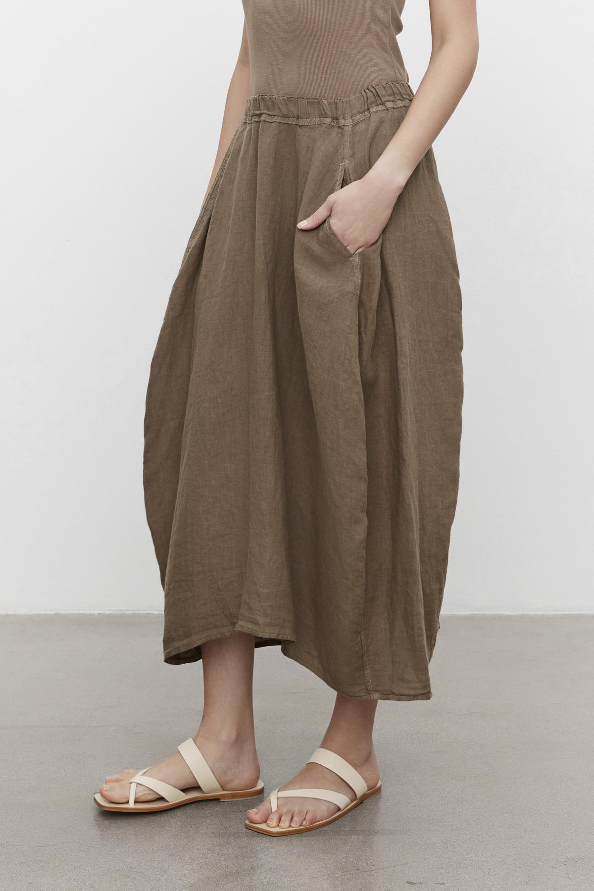 A person wearing a Velvet by Graham & Spencer FAE Linen A-Line Skirt with an elastic waistband and sandals against a plain background.-36443407122625