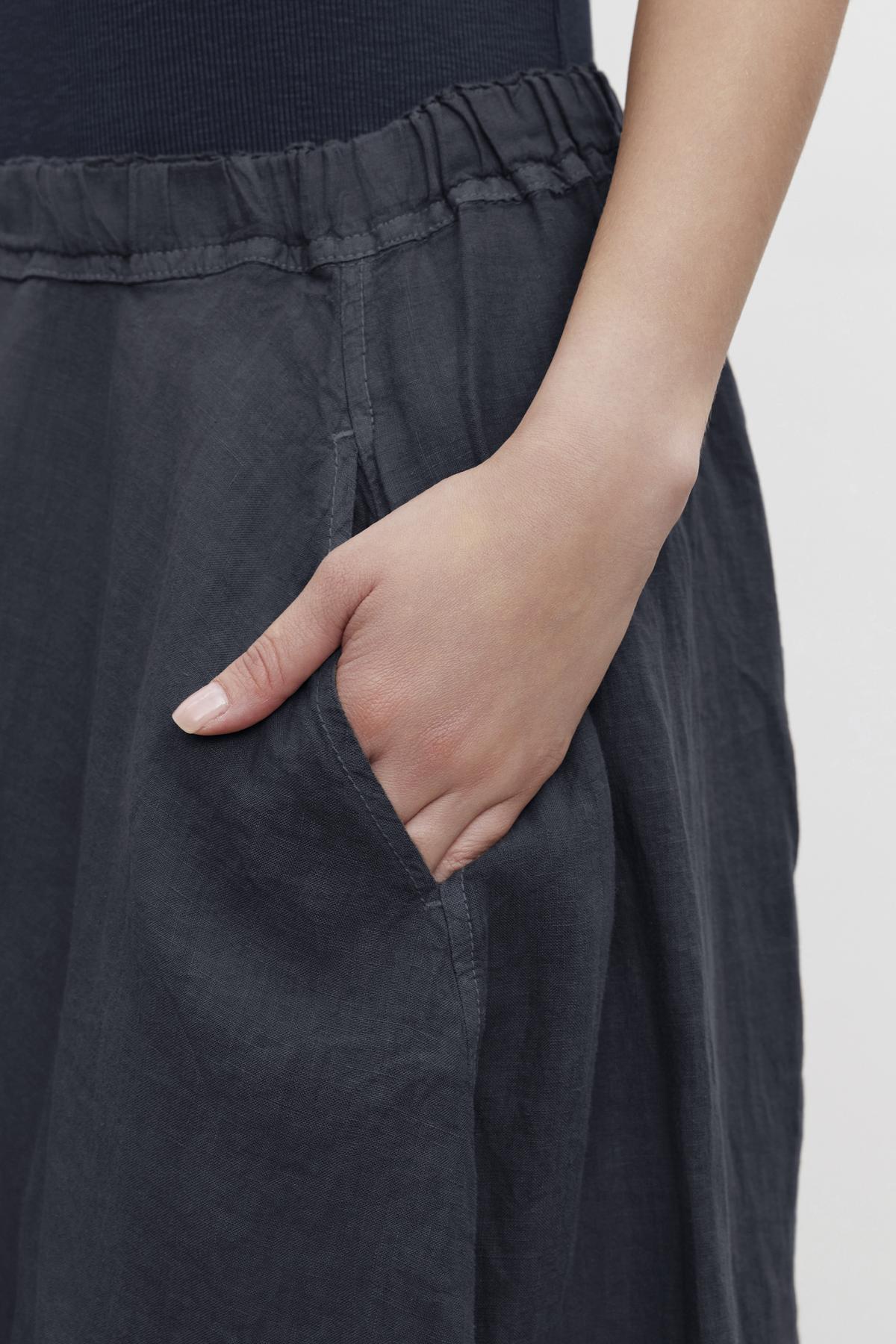   Close-up of a woman's hand with a white fingernail, partially inserted into the pocket of her Velvet by Graham & Spencer FAE LINEN A-LINE SKIRT. 