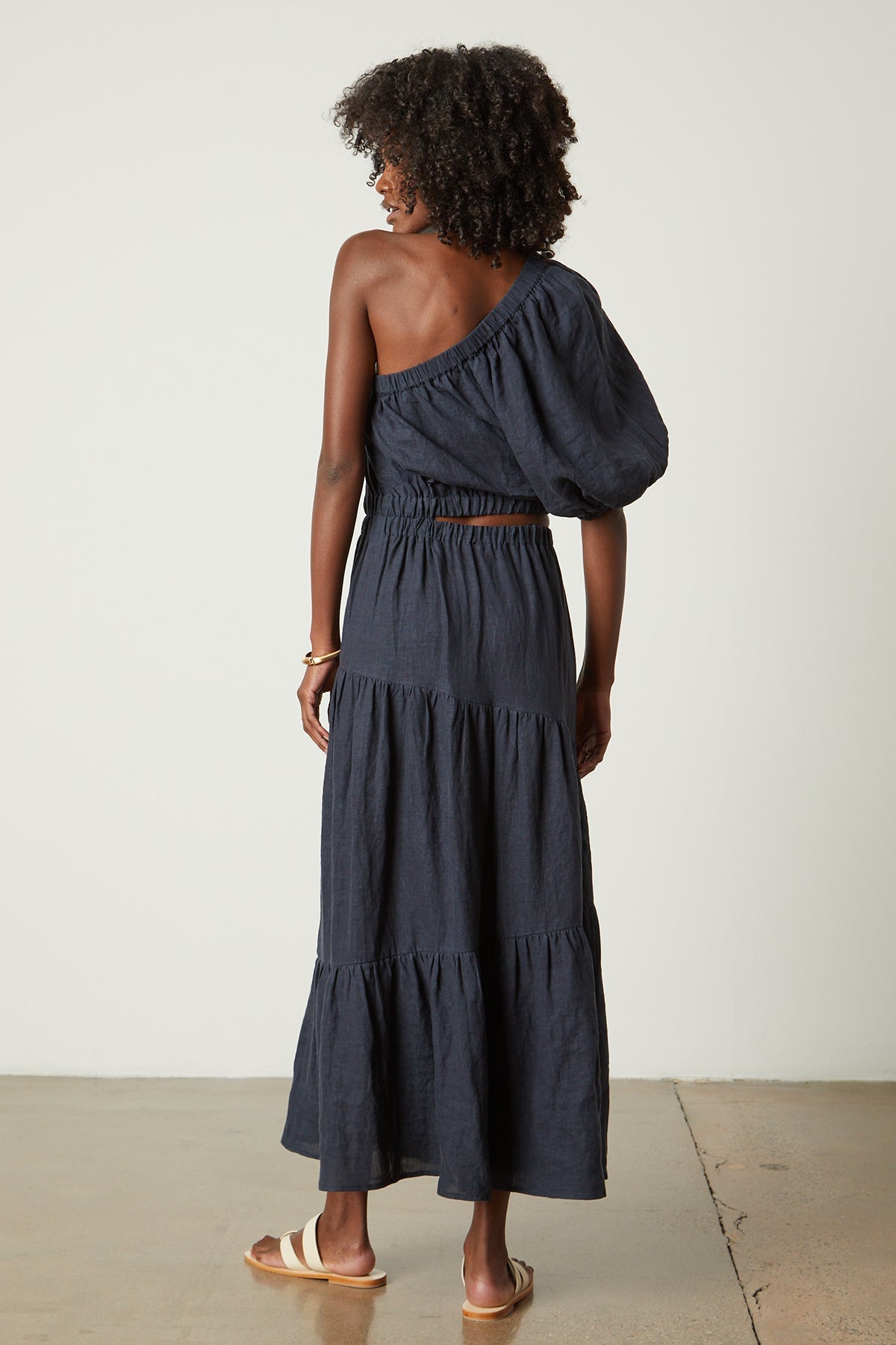   the back view of a woman wearing a Velvet by Graham & Spencer GISELLE LINEN ONE SHOULDER DRESS in navy. 