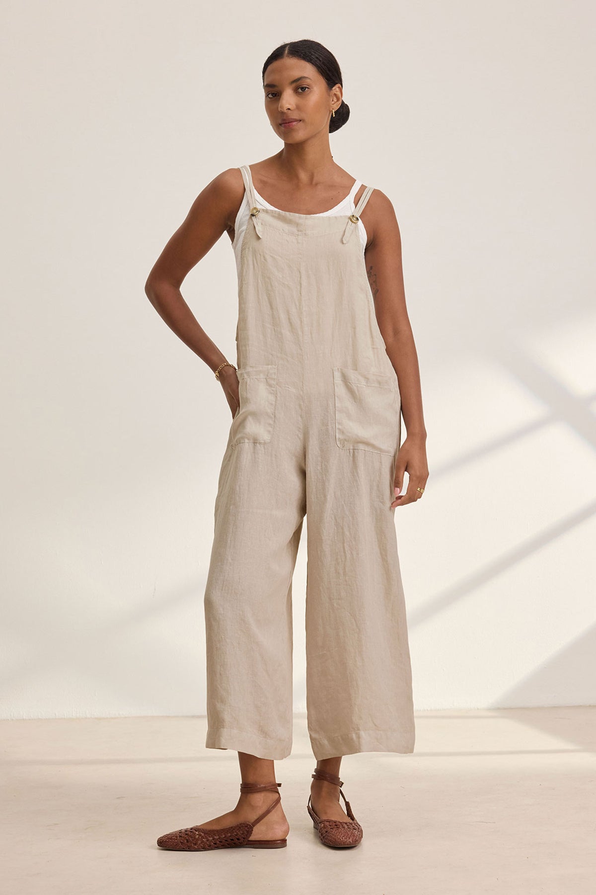 A person wearing the ISABEL LINEN ROMPER by Velvet by Graham & Spencer and brown sandals stands against a plain background, epitomizing relaxed and versatile style with a neutral expression.-38890941120705