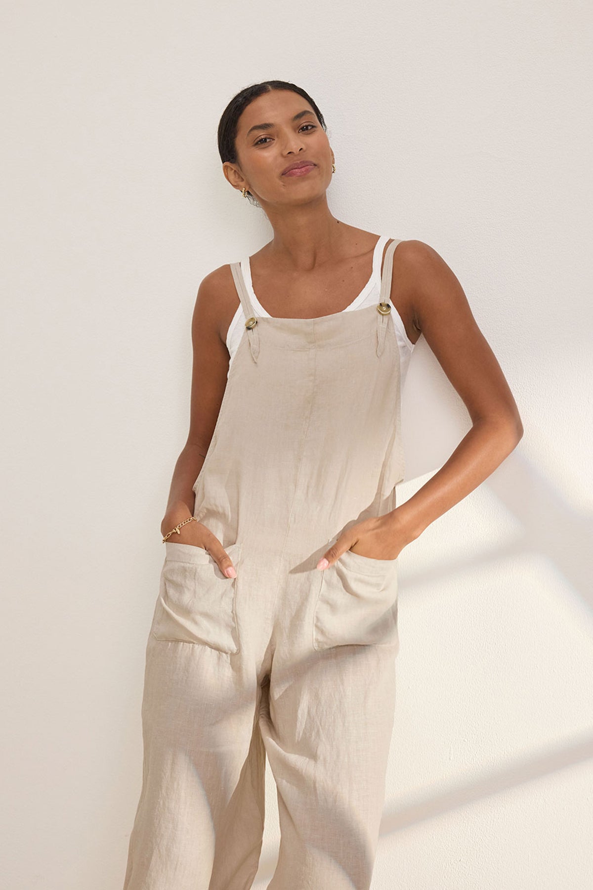 A person models the ISABEL LINEN ROMPER by Velvet by Graham & Spencer, styled over a white tank top against a light background. With hands in pockets, it exudes relaxed and versatile style—ideal for warm weather.-38890941350081