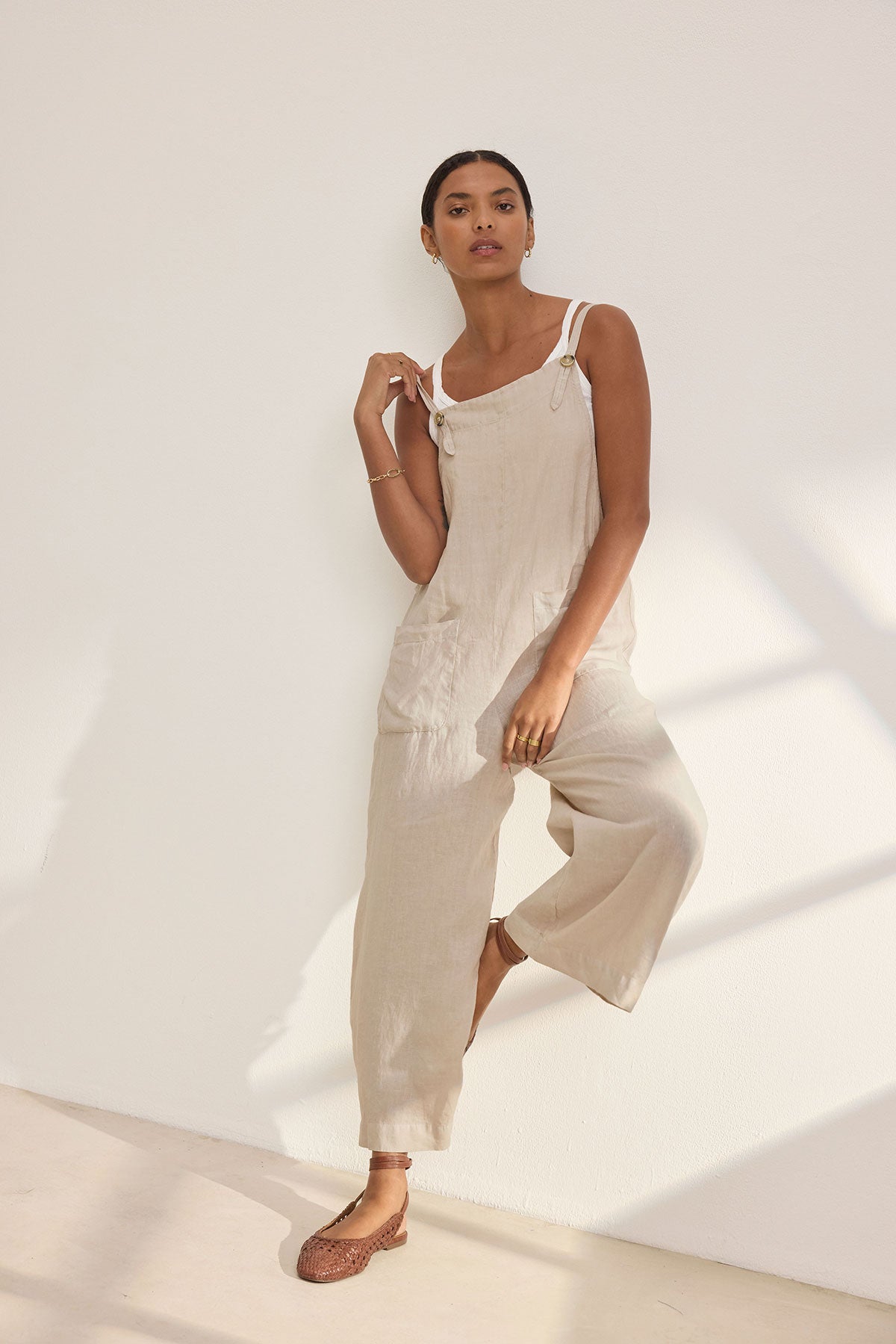 Wearing the ISABEL LINEN ROMPER by Velvet by Graham & Spencer, a person showcases relaxed versatility against a sunlit white wall.-38890941382849
